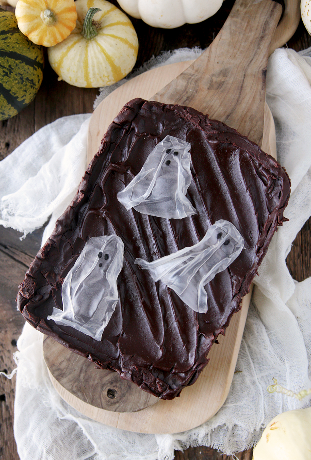 frosted brownies with rice paper ghosts on brownies with mini pumpkins next to brownies